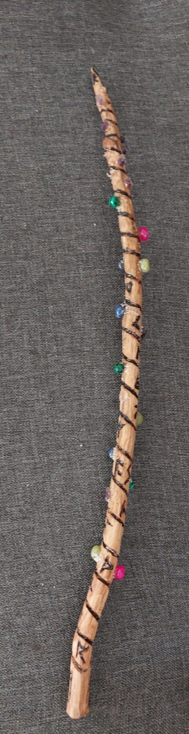 Bild eines aus Holz geschnitzten Zauberstabes mit eingeschnitzten Runen und angebrachten Halbedelsteinen