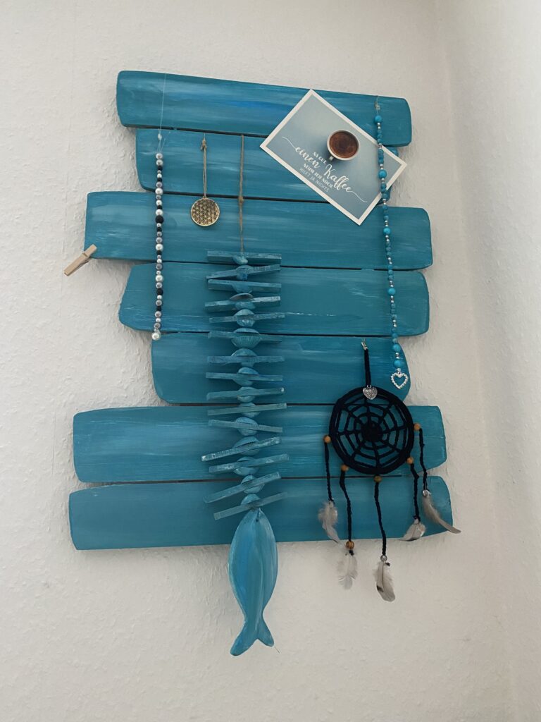 Bild eines Kunstobjektes in Türkusmit Traumfänger, verschiedenen Hängern und einer Postkarte